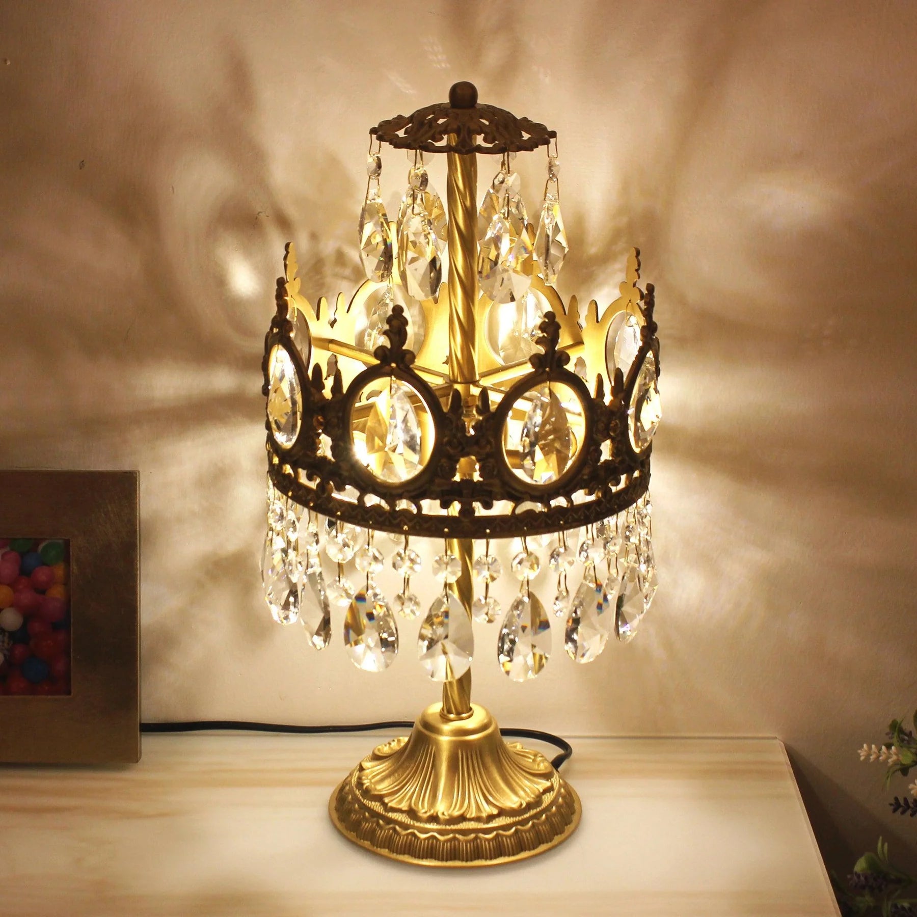 Vintage crystal table lamp with ornate gold base and hanging glass prisms on a light surface